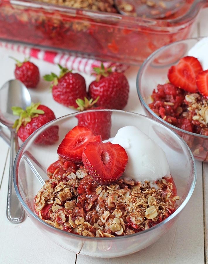 Rhubarb and strawberry crisp in a small glass bowl garnished with ice cream and fresh strawberries.