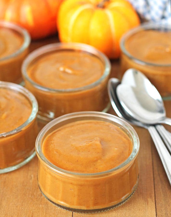Pumpkin pie pudding in glass serving jars on a brown wood table.