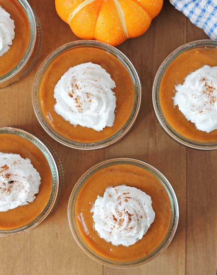 Overhead shot of dairy free pumpkin pie pudding cups sitting on a brown wood table.