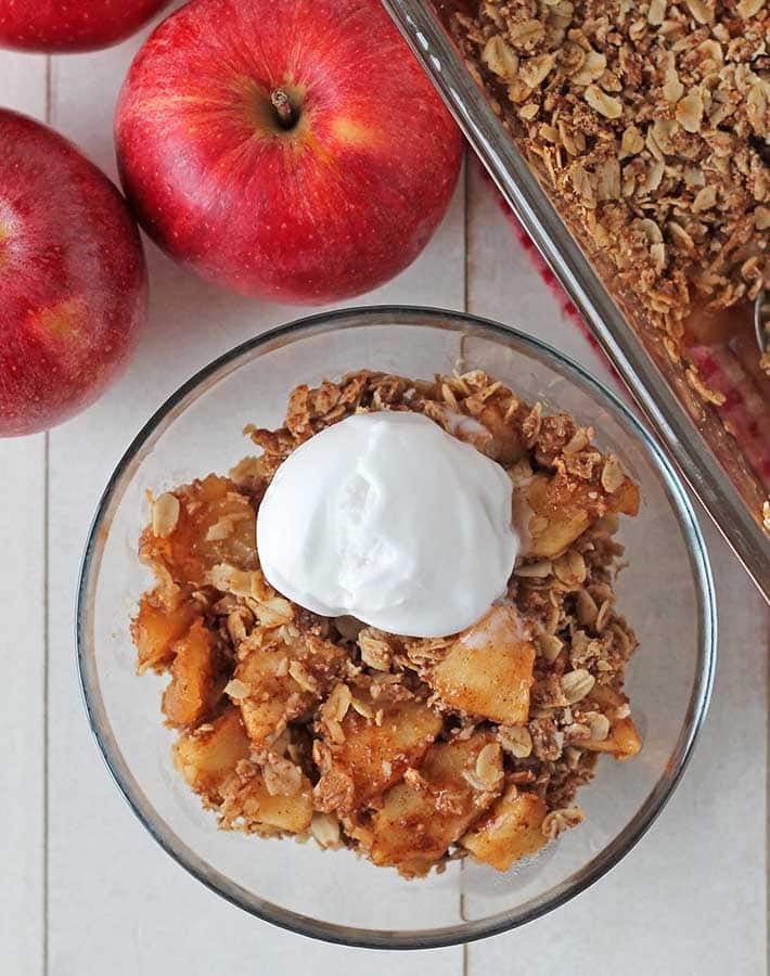 Overhead shot of vegan apple crisp in a small bowl, crisp is topped with a scoop of ice cream.