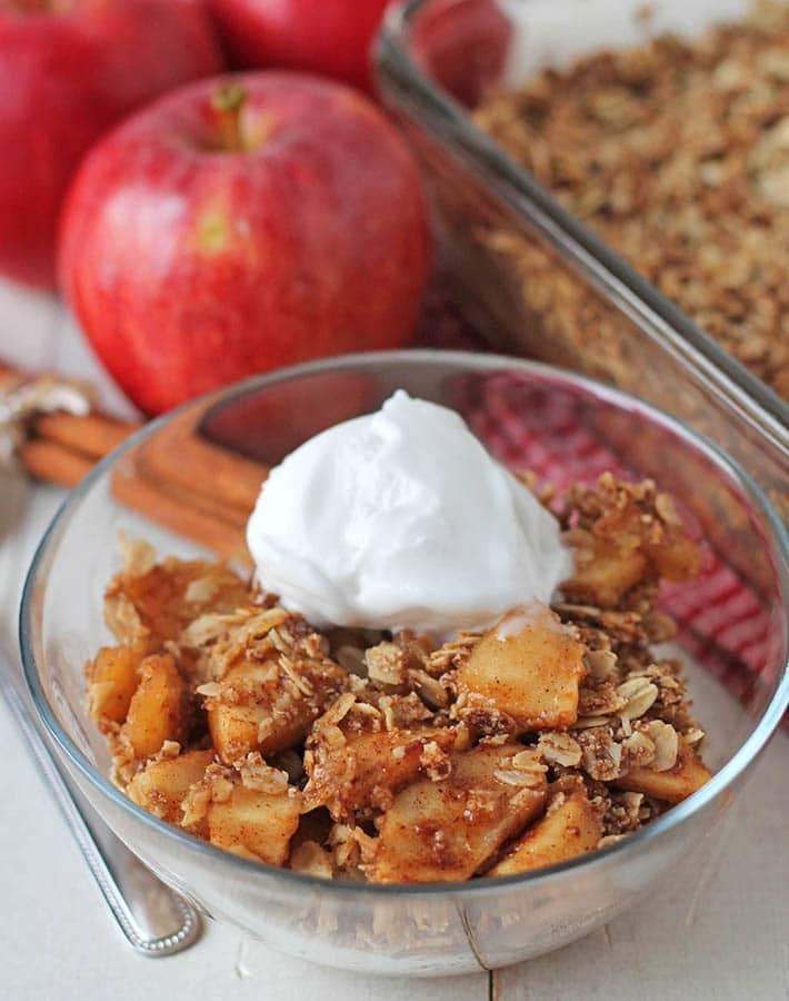 Non dairy apple crisp in a small glass bowl with a scoop of coconut ice cream on top.