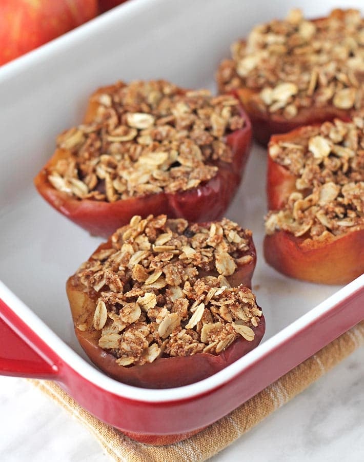 Four baked apple halves in a red and white baking dish.