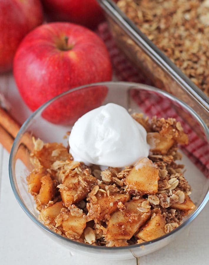 Vegan apple crisp in a bowl, bowl is sitting on a white table.