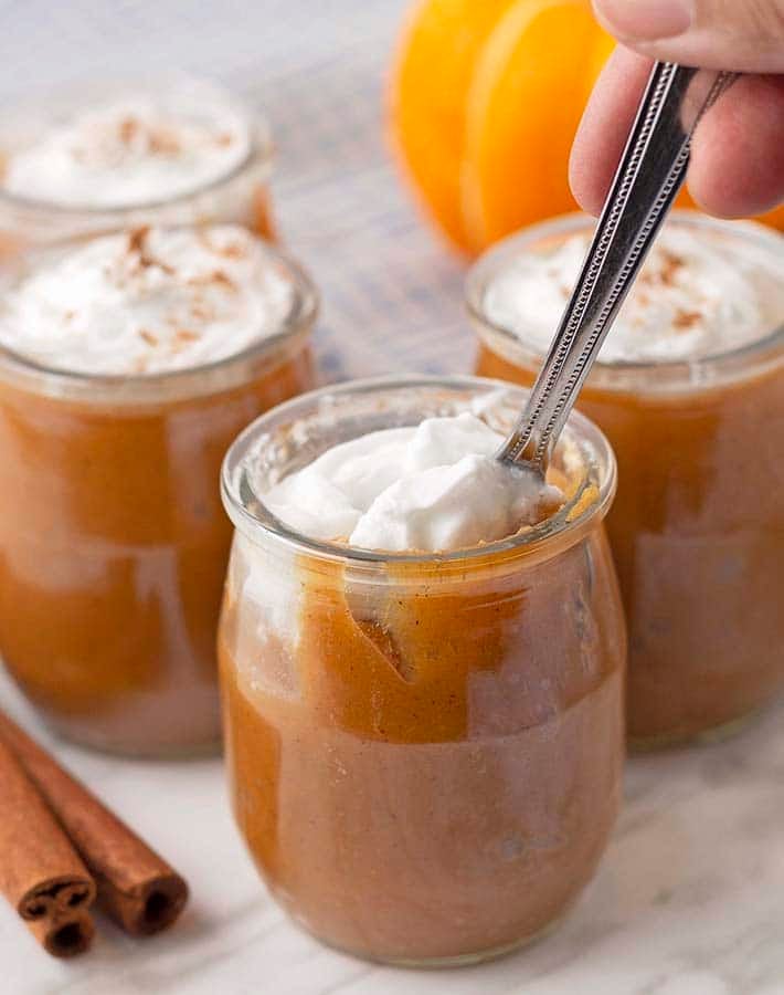 A glass jar with vegan pudding, it is topped with coconut whipped cream and a spoon is in the jar.