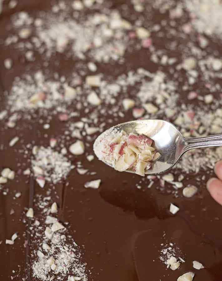 A spoon sprinkling crushed candy cane onto melted chocolate to make peppermint chocolate bark.
