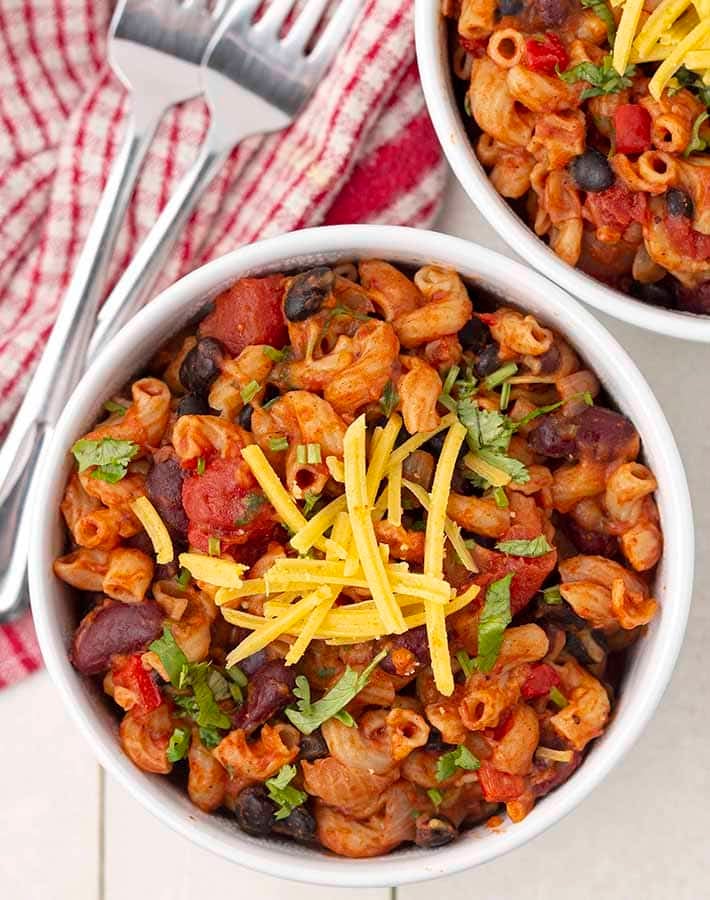 Overhead shot of two bowls of vegan chili mac on a white wood table.