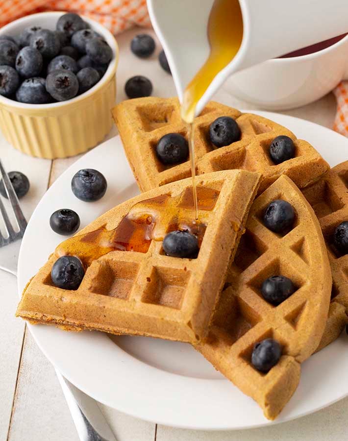 Syrup being poured onto a stack of vegan sweet potato waffles.