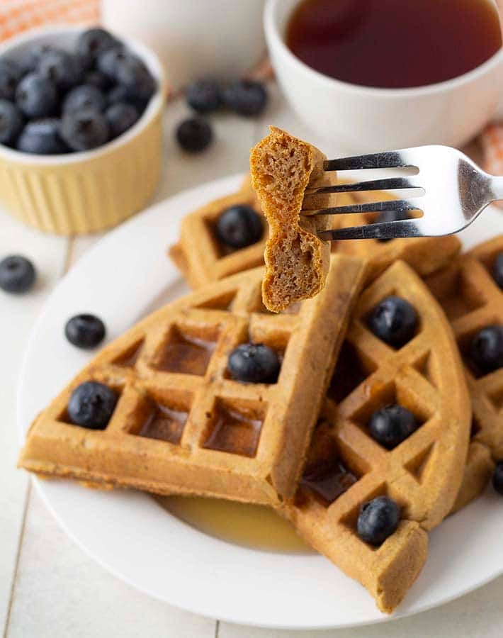 A fork holding up a piece of a gluten free sweet potato waffle to show the inner fluffy texture.