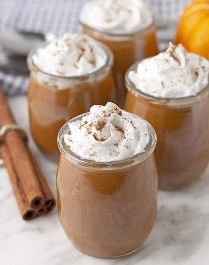 Four jars with sweet potato pudding topped with coconut whipped cream.
