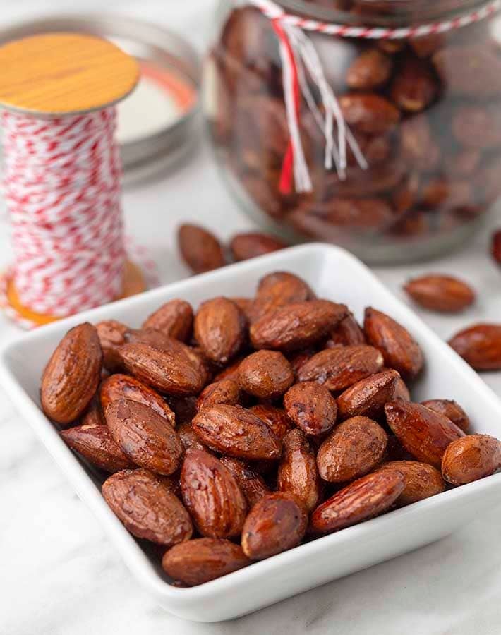 Cinnamon spiced almonds in a small dish, a jar of more almonds sits behind.