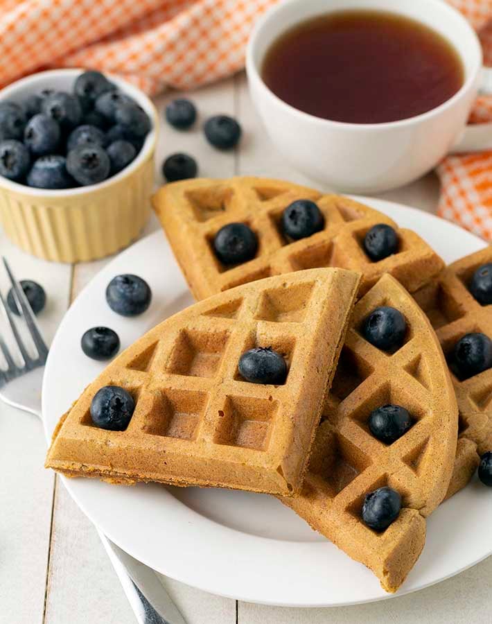 A plate of sweet potato waffles on a white plate, waffles are garnished with fresh blueberries.