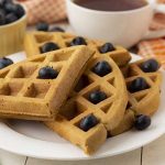 Close up shot of a plate of gf sweet potato waffles that are garnished with fresh blueberries..