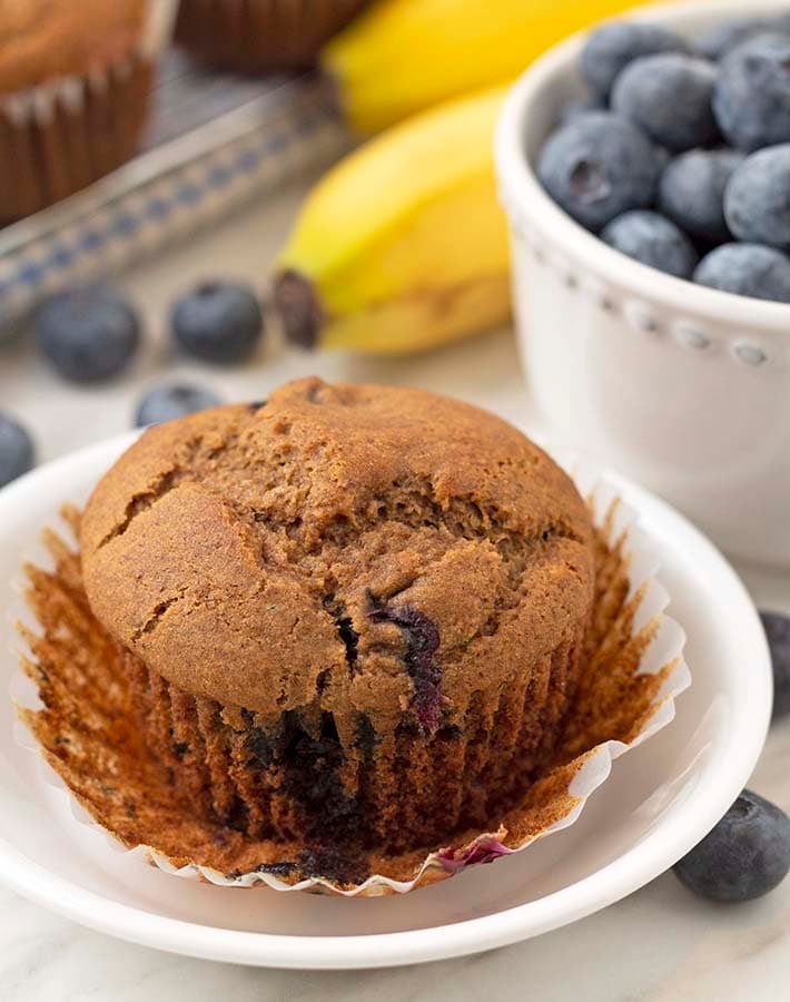 Close up shot of a gluten free banana and blueberry muffin on a plate with the muffin wrapper peeled off.