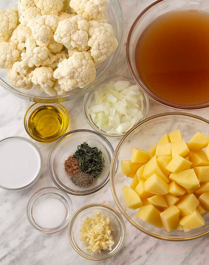 Overhead shot of ingredients needed to make vegan cauliflower and potato soup, all ingredients are in separate glass bowls.