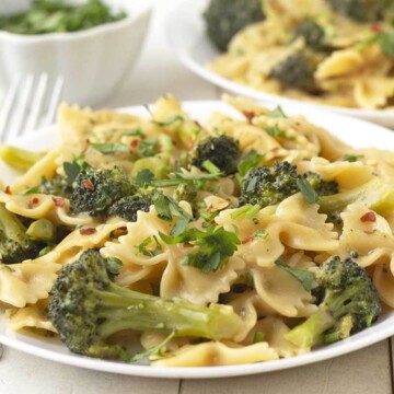 Creamy vegan broccoli pasta on a white plate, two forks sit to the left of the plate.