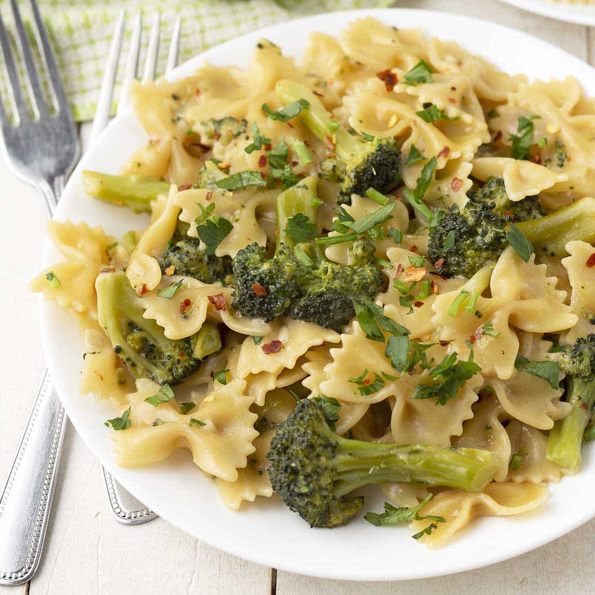 Close up shot of a plate of bow tie pasta and broccoli, two forks sit to the left of the plate.