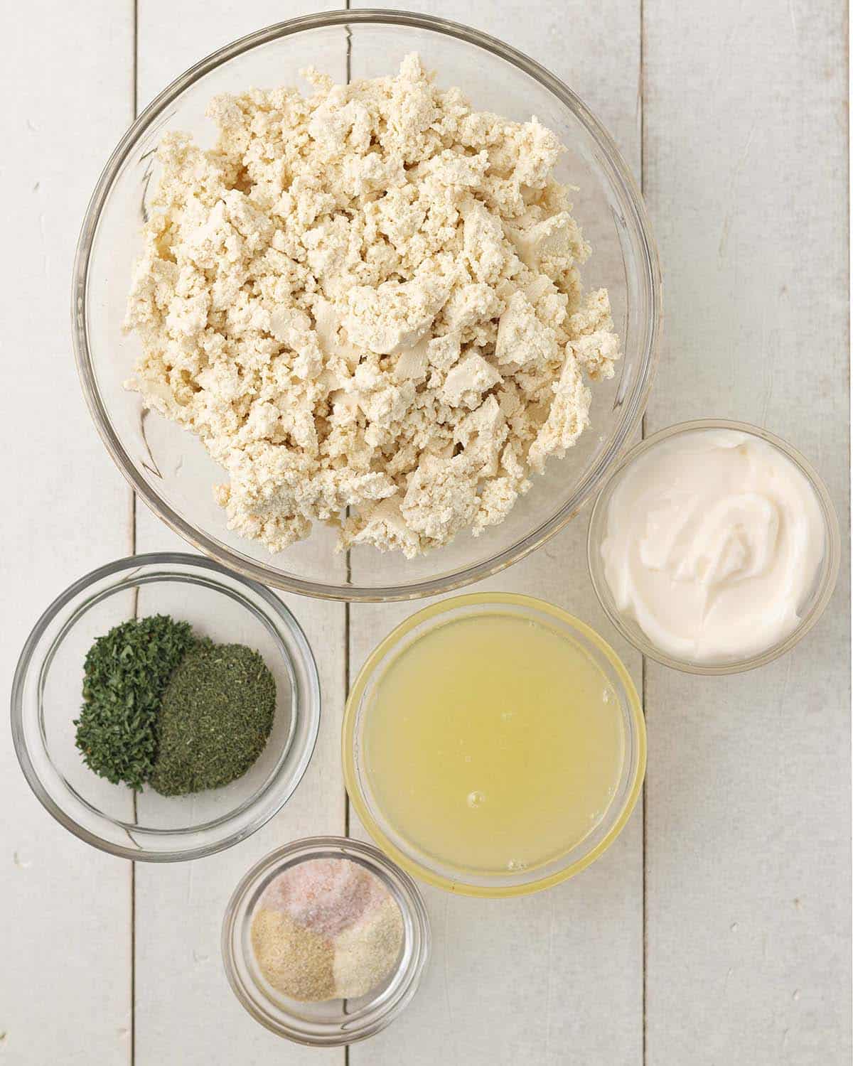 An overhead shot of glass bowls, each filled with the ingredients needed to make vegan dill dip.