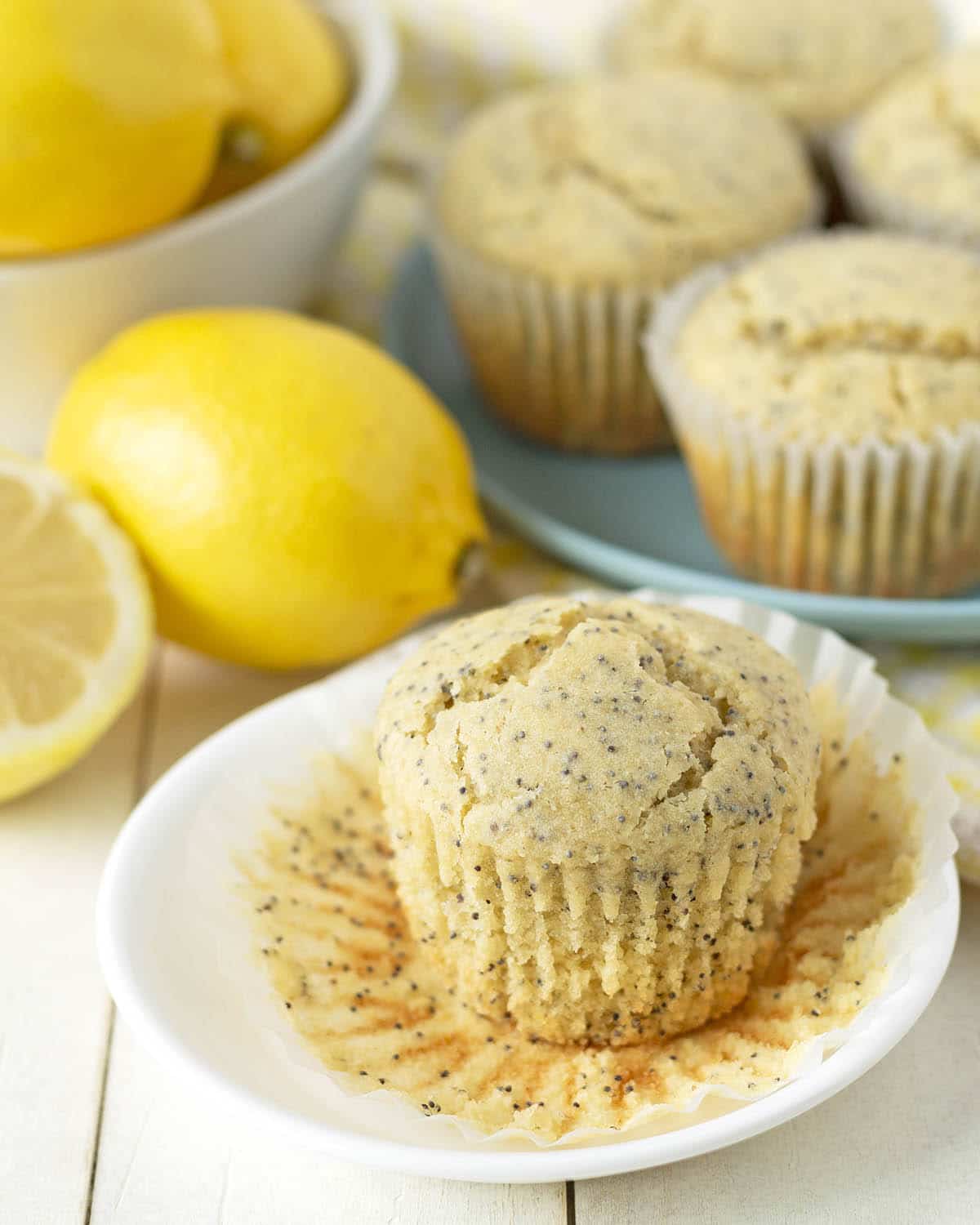 A vegan lemon poppy seed muffin on a white plate with the paper wrapper peeled off.