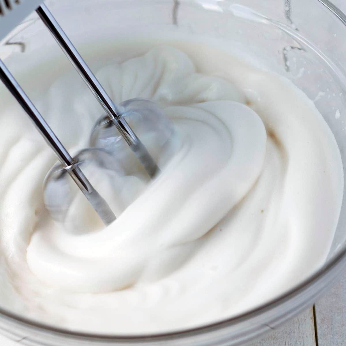 Close up image of aquafaba being whipped with a hand mixer in a glass bowl.