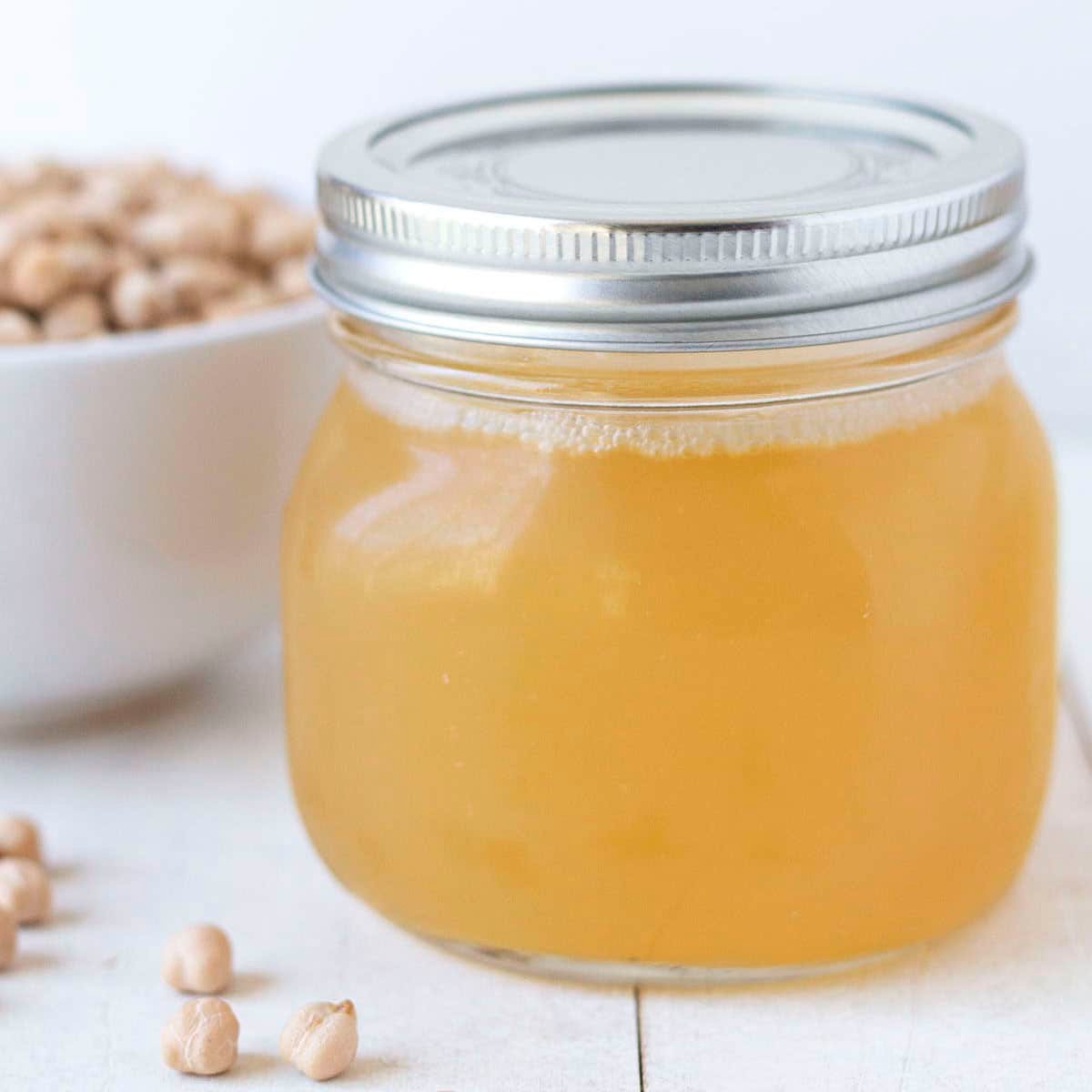 A mason jar of homemade aquafaba egg replacement sitting on a white wooden table.