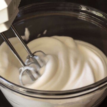 Image shows a bowl of aquafaba being whipped with a hand mixer.