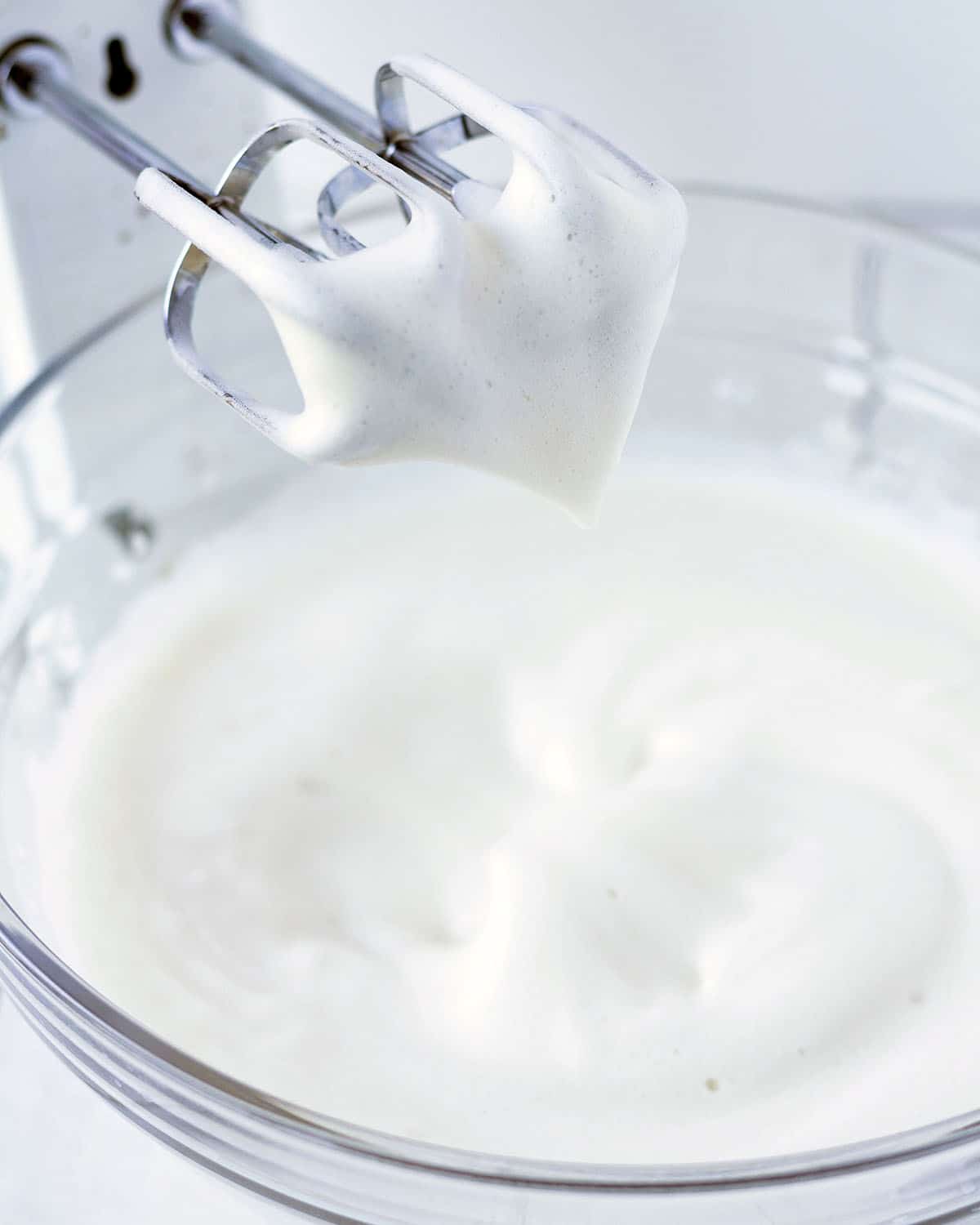 Image shows a hand mixer with a bowl of whipped aquafaba that has reached soft peak stage.