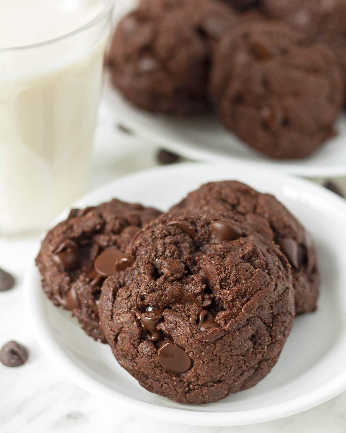 Three vegan double chocolate chip cookies sitting on a small white plate.