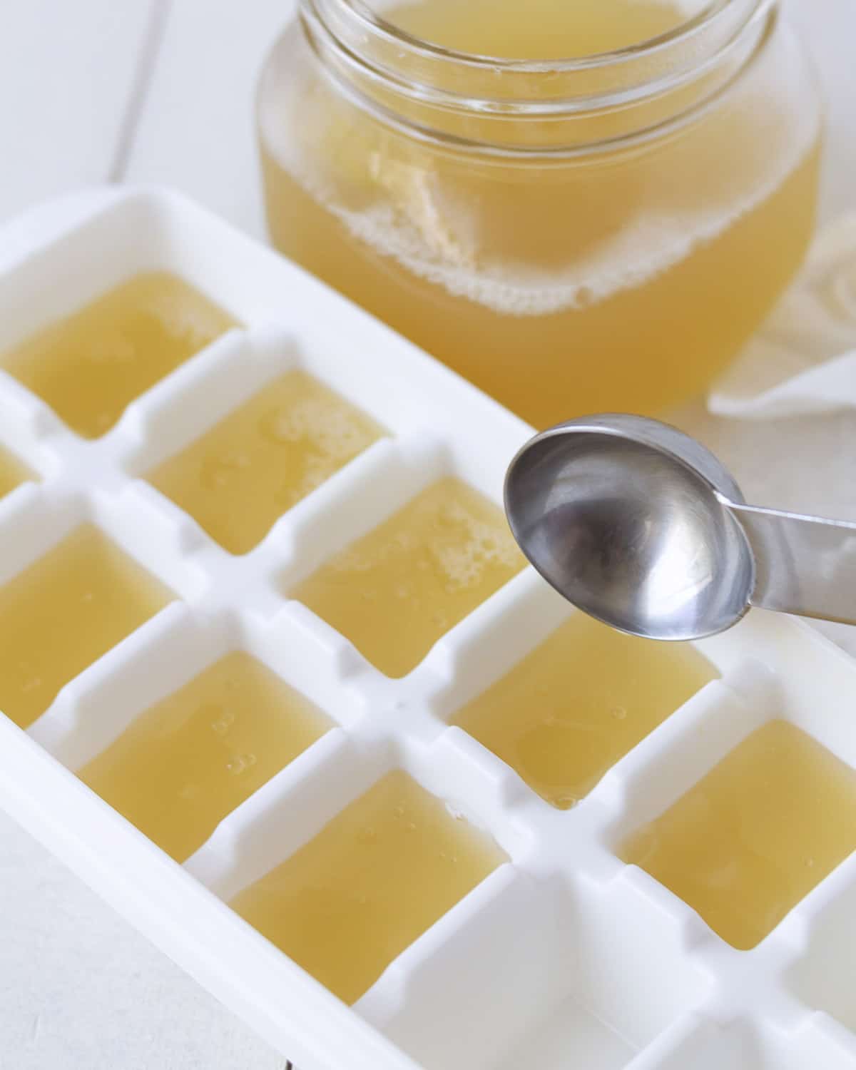 A tablespoon measure adding homemade aquafaba to an ice cube tray for freezing.