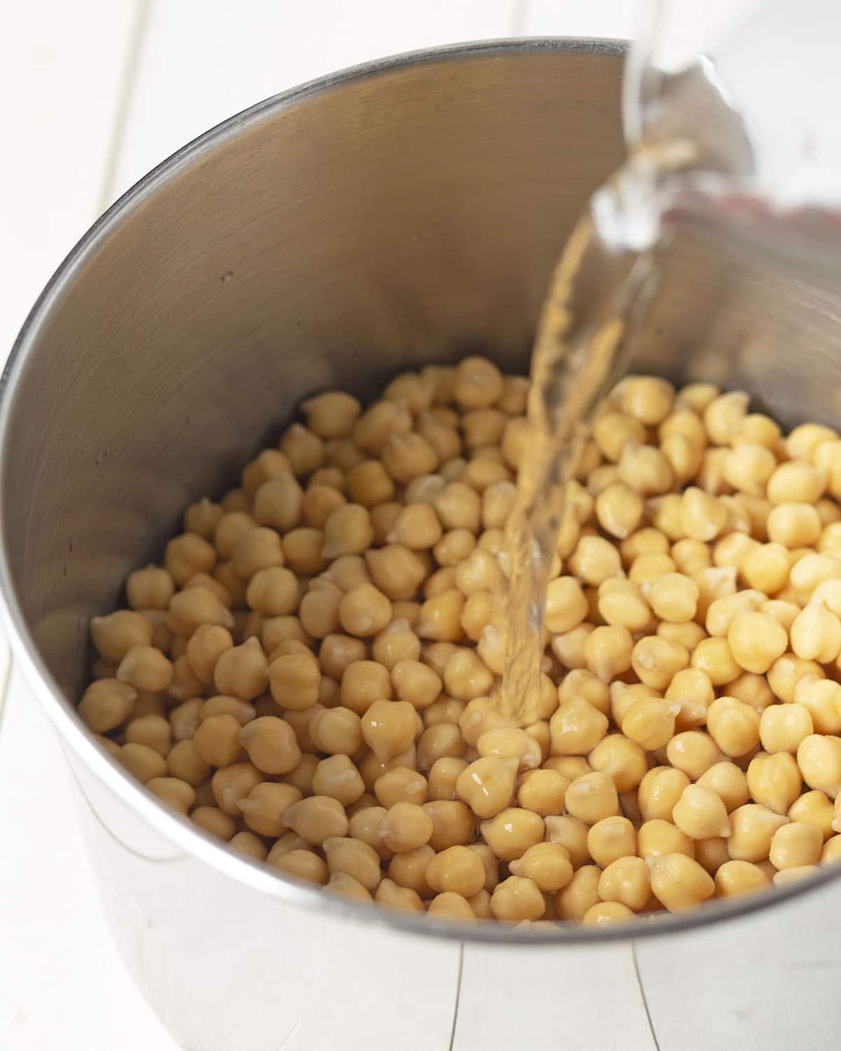 Chickpeas in a pot, water is being poured on top of the chickpeas.