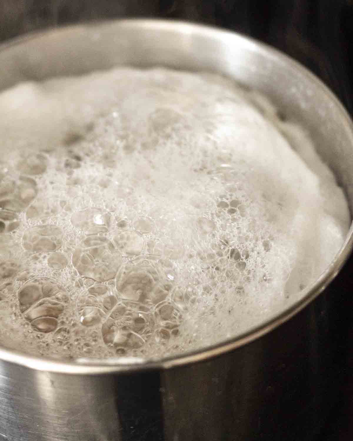 Image shows a pot of boiling chickpeas, the chickpeas are covered with a white foam that forms when chickpeas boil.