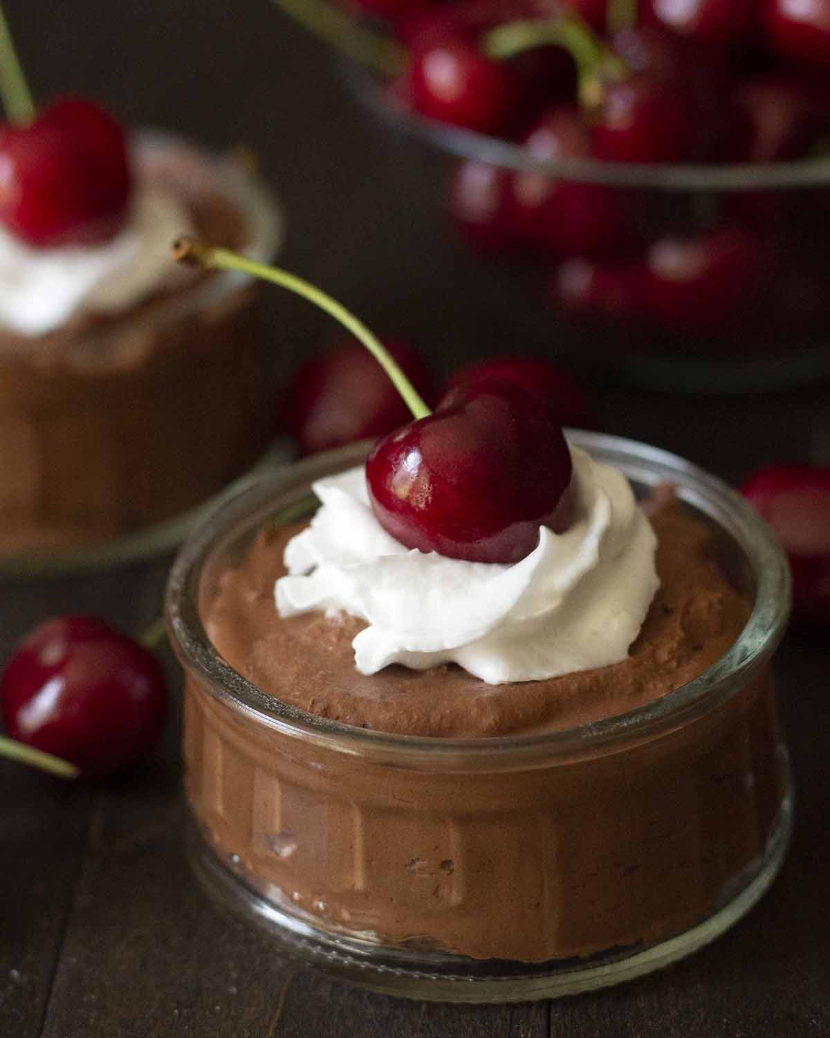 A vegan chocolate dessert in a glass bowl topped with dairy-free whipped cream and a fresh cherry.