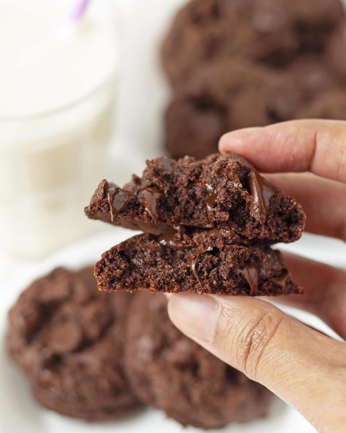 A close up shot of a hand holding a chocolate cookie split in two to show the inner texture.