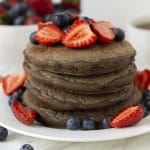 A stack of four gluten free buckwheat pancakes on a plate, pancakes and plate are decorated with fresh berries.
