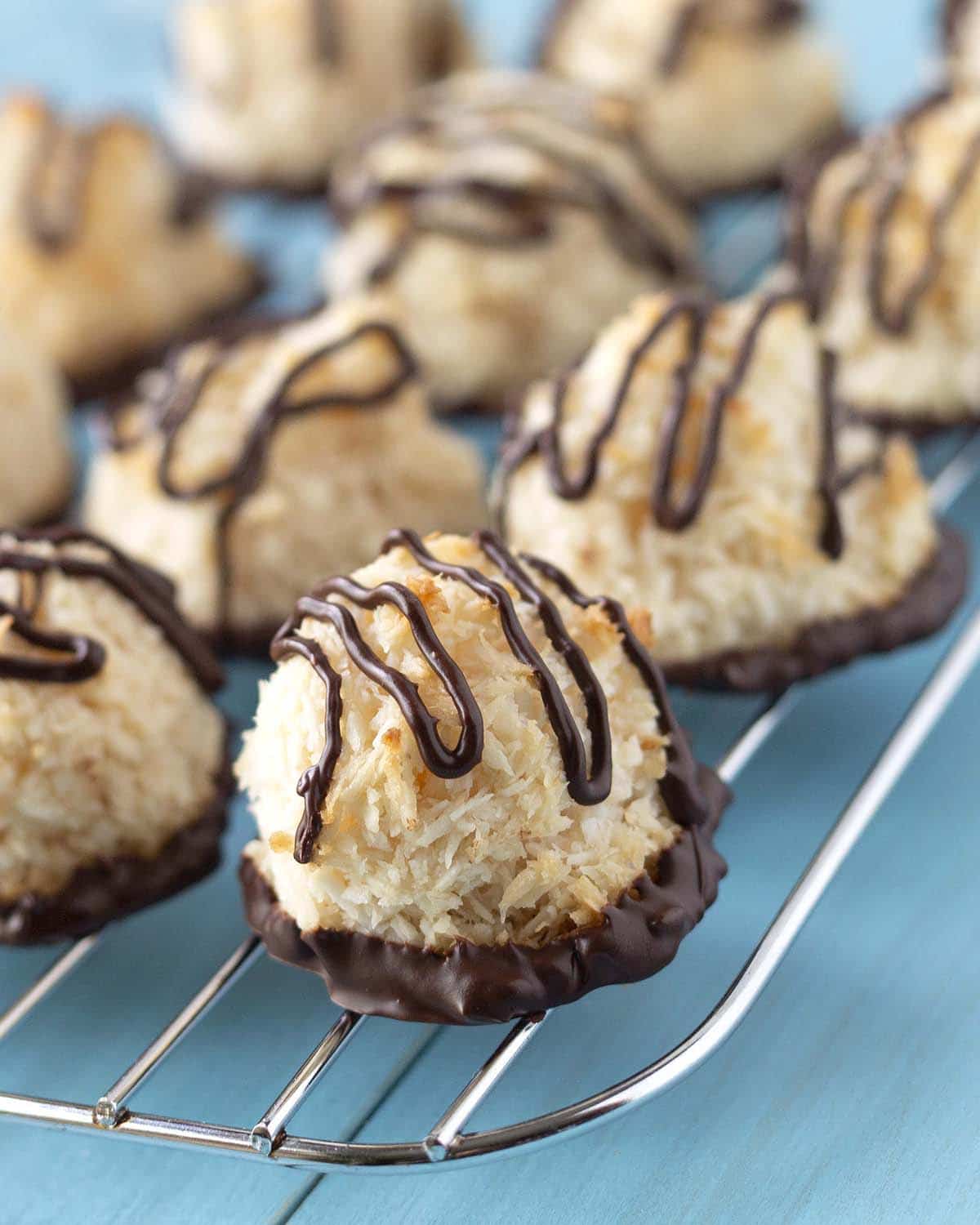 Coconut aquafaba macaroons sitting on a cooling rack, the cooling rack is sitting on a blue surface.