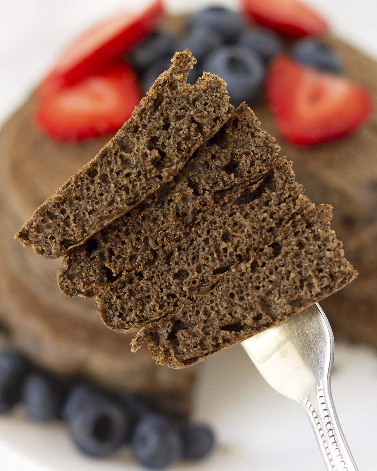 A fork holding up a cross section of fluffy buckwheat pancakes to show how fluffy they are on the inside.