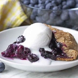 A slice of gluten free blueberry galette on a white plate with a scoop of coconut ice cream on top.