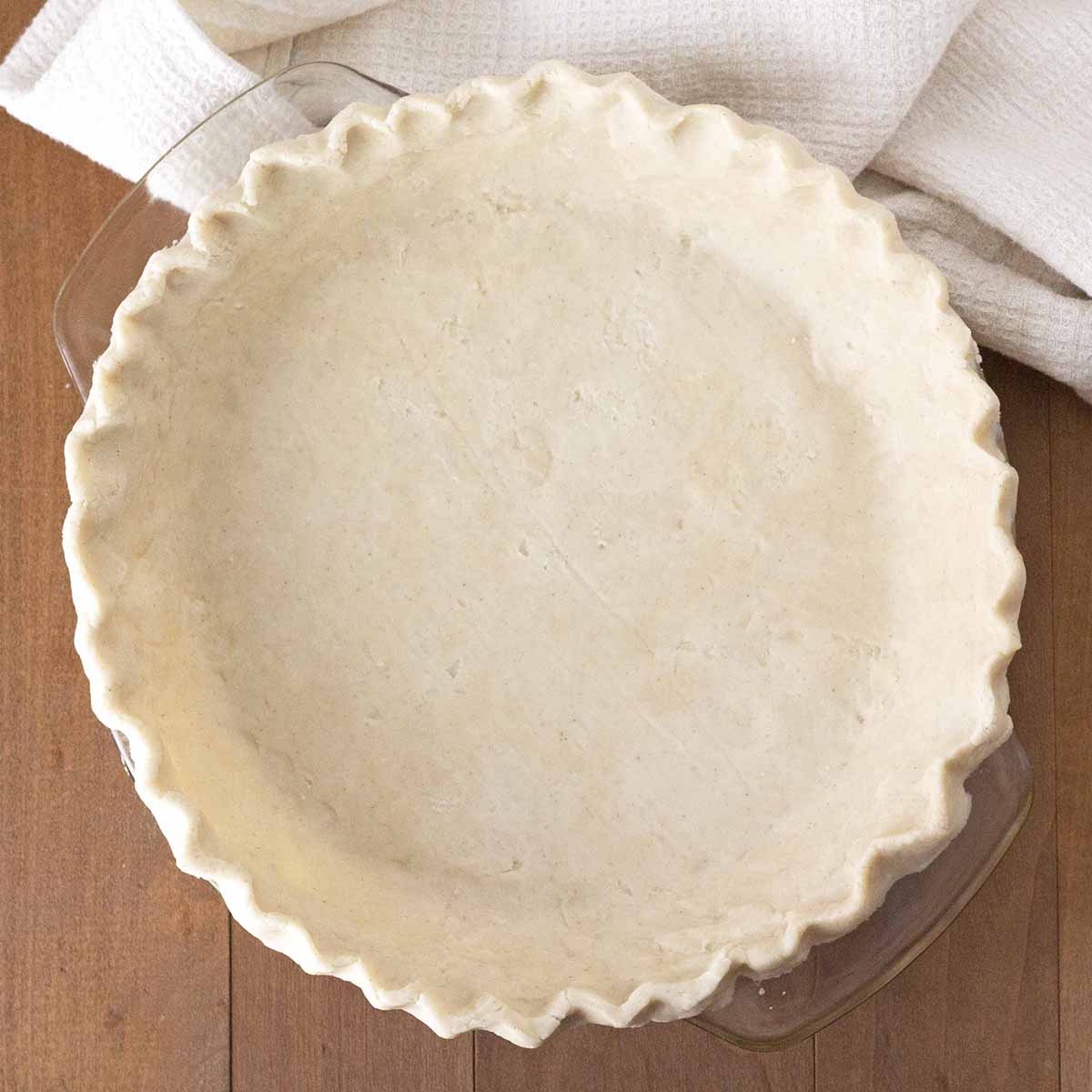 An overhead shot of a finished crust for pie in a glass pie dish.