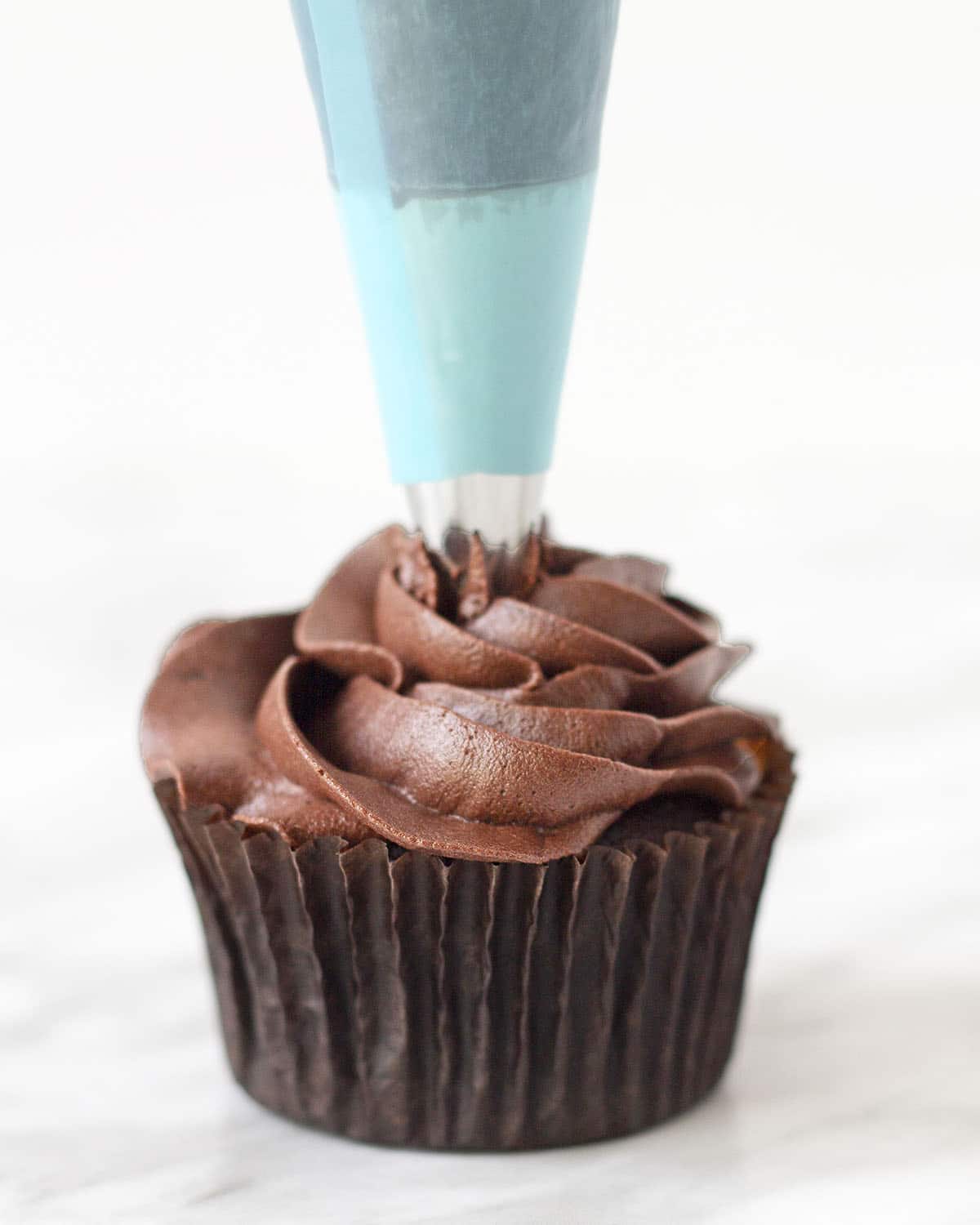 Dairy-free chocolate icing being piped onto a chocolate cupcake.