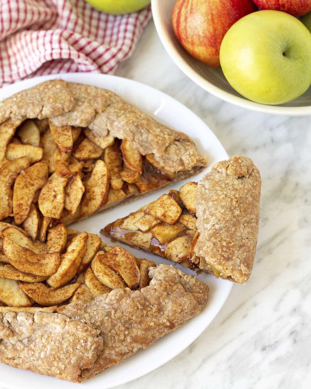 An overhead shot of a vegan apple galette on a white dish, one slice is pulled out and away from the galette.