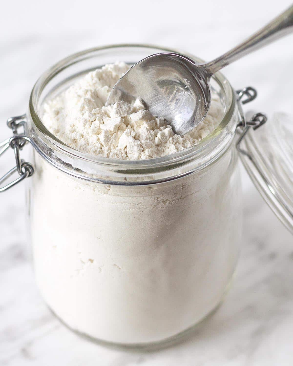 A spoon in a jar of flour, the spoon is fluffing the flour up before scooping it out for measuring.