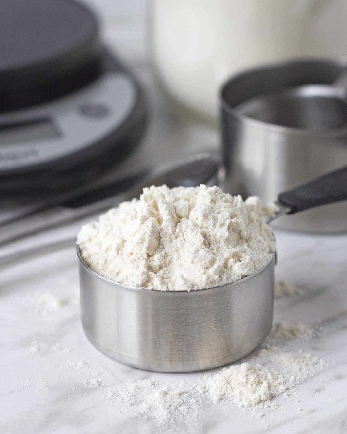 A measuring cup filled with flour, cup is sitting on a marble counter surface.