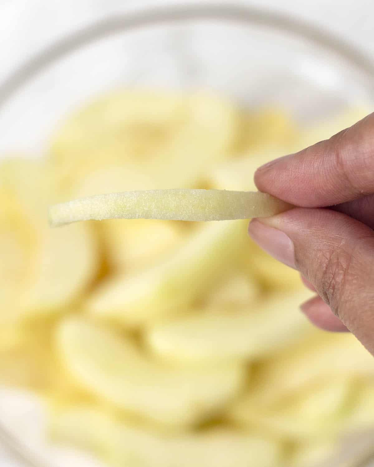 A close up shot of a hand holding a slice of apple to show how thick the apples should be sliced for this recipe.