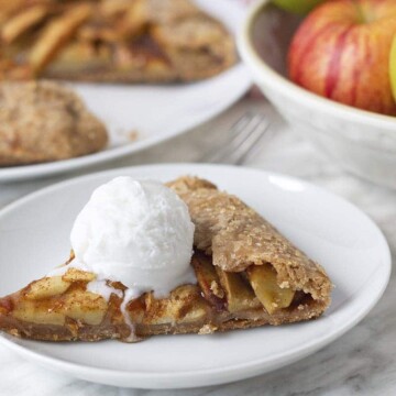 A slice of gluten free apple galette on a white plate with a scoop of coconut ice cream on top.
