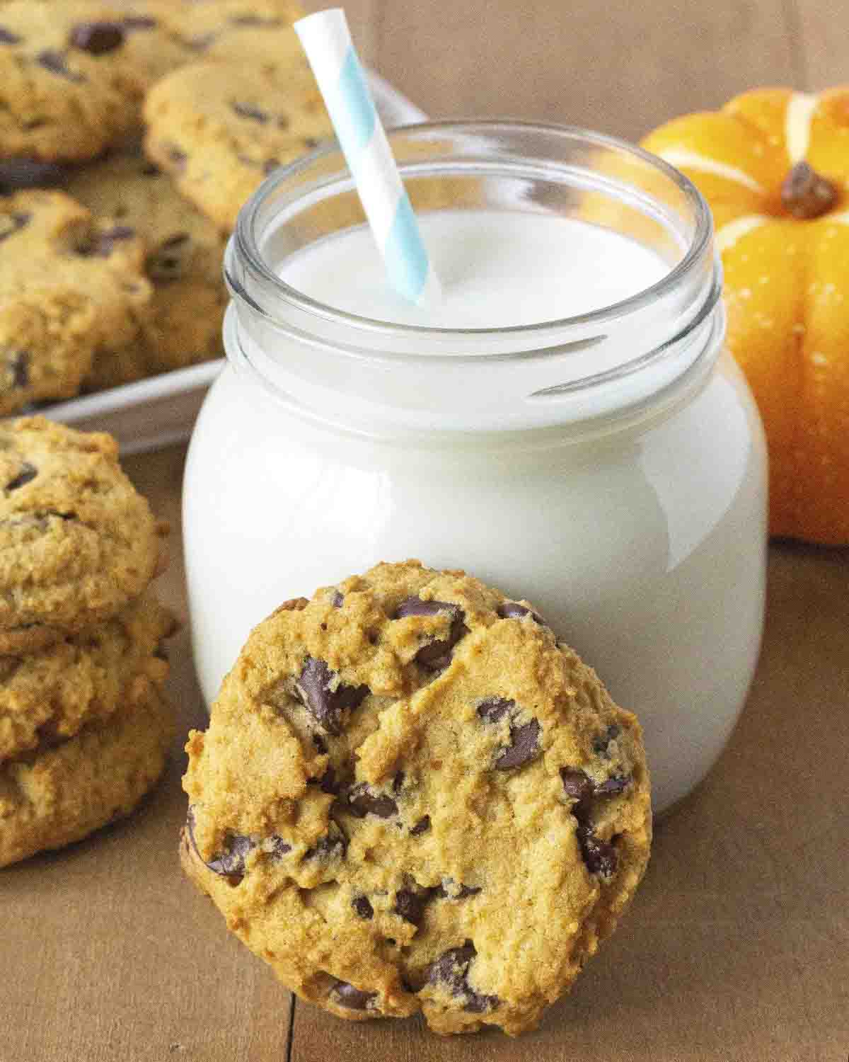 A single pumpkin chocolate chip cookie leaning on a glass of almond milk.