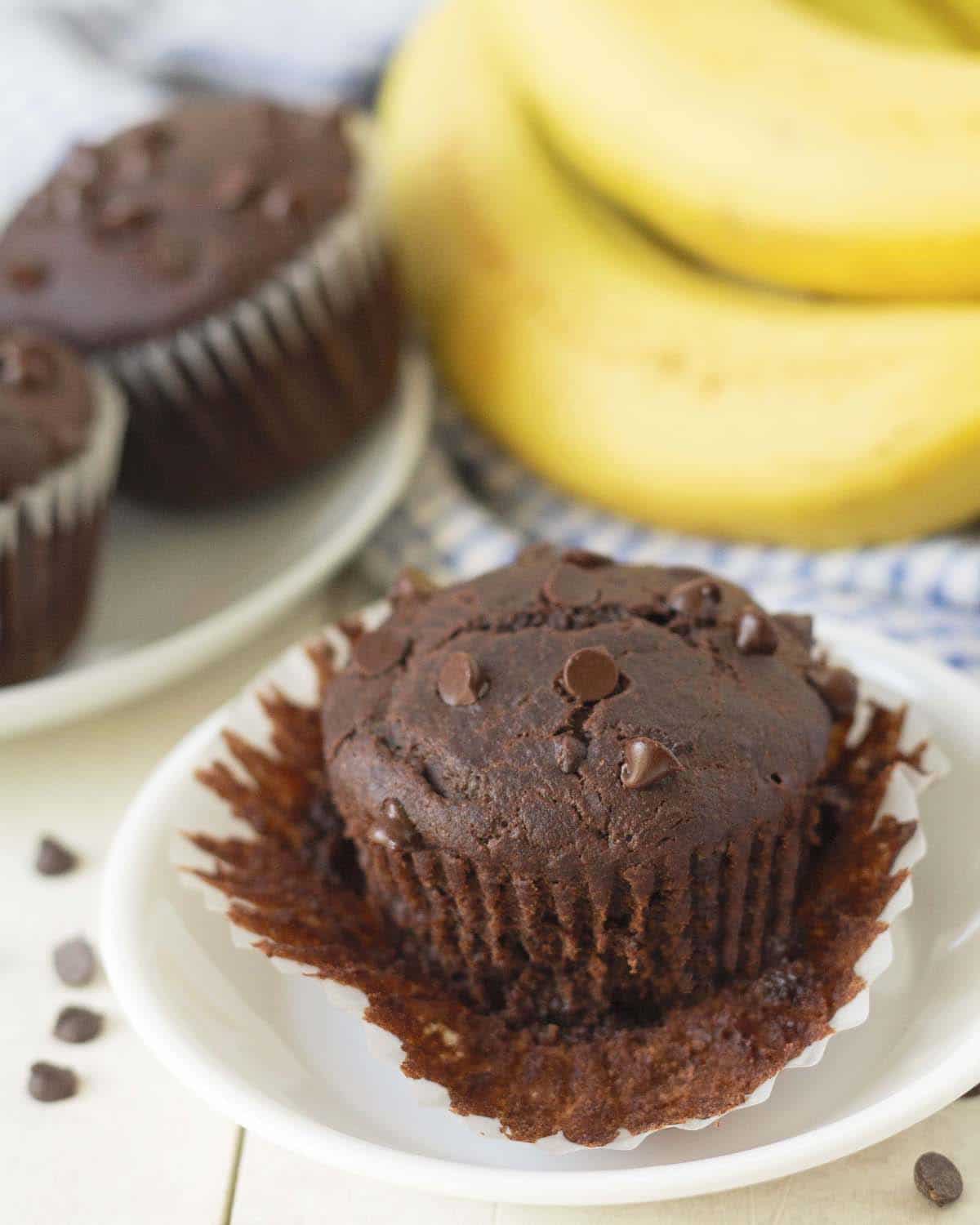 An egg-free, dairy-free chocolate banana muffin on a plate with the muffin wrapper peeled down.