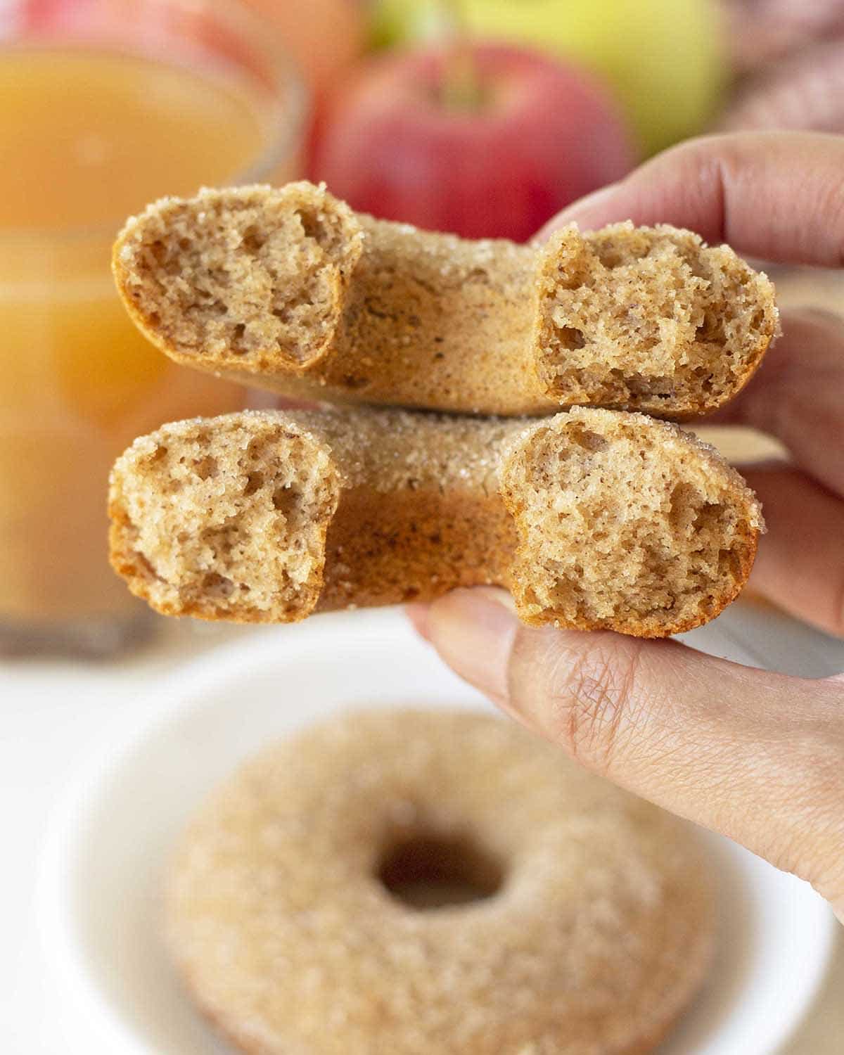 A hand holding half of a vegan and half of a vegan gluten free apple cider donut to show the inner fluffy textures.
