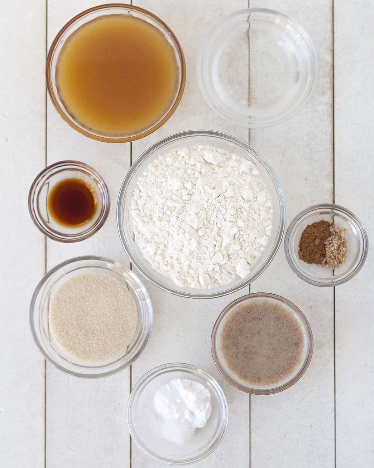 Image showing all the ingredients needed to make baked gluten-free apple cider donuts, all ingredients are in separate bowls.