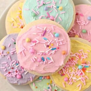 An overhead shot of colourful buttercream frosted sugar cookies with sprinkles on a plate.