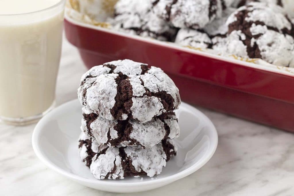 Three eggless chocolate crinkle cookies on a small white plate, stacked on top of each other.