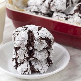 Three eggless chocolate crinkle cookies on a small white plate, stacked on top of each other.
